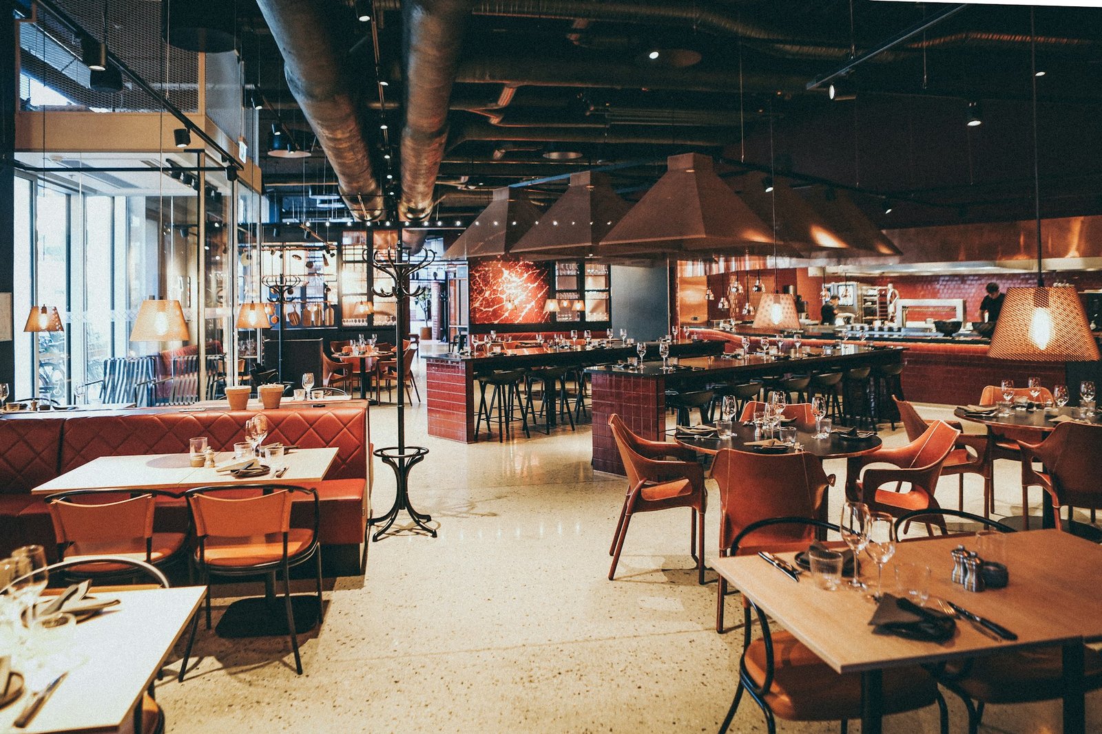 Sala de un restaurante con mesas preparadas, lámparas colgantes y barra al fondo